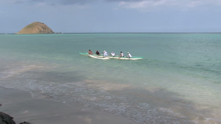 Tropical beach on Oahu, Hawaii. Islands off shore in Pacific ocean. Outrigger paddling away from beach towards another island. Waves on white sand. Scenic, relaxing, calm seascape.
