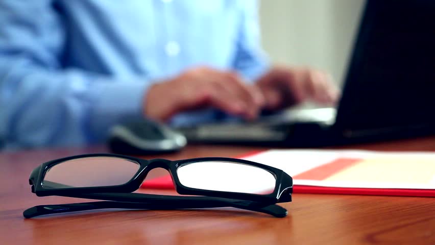 Businessman typing on a laptop, focus on glasses