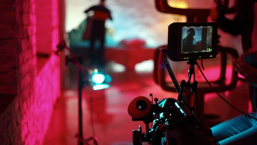 operator cleans lens of professional videocamera, and on background scenery are prepared