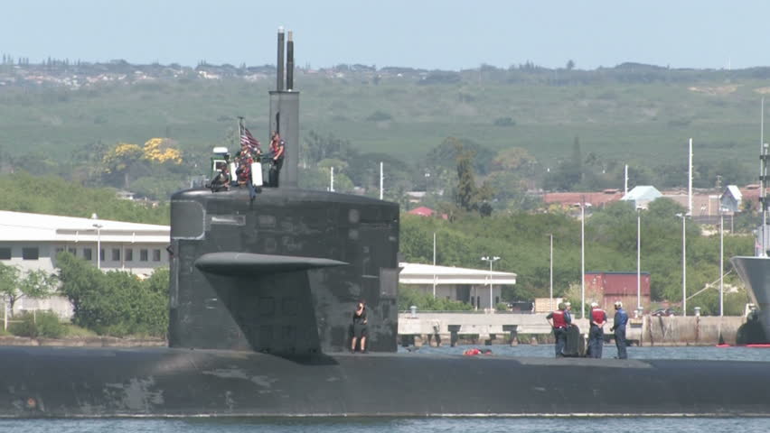 US Navy person-ell on deck of submarine in Pearl Harbor,  Honolulu, Oahu, Hawaii. Floating slowly in ocean bay with crew members on its deck and conning tower. 