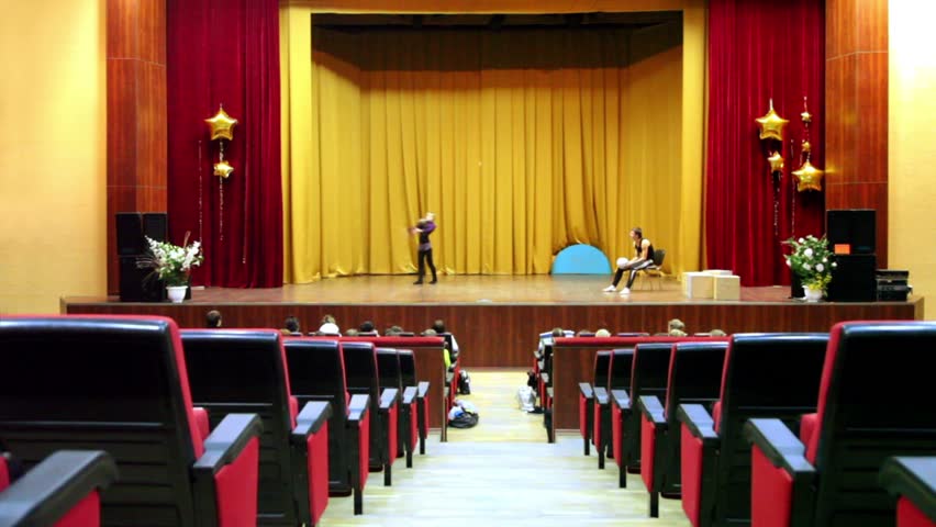 Girl make tricks with ball on theater scene, boy sit on chair, people watch acting classes at Institute of Sports