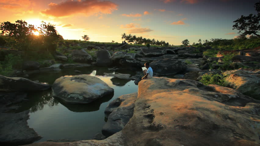 A child sitting on a rock near a village in Kenya two hours north of the African city Mombassa at sunset.