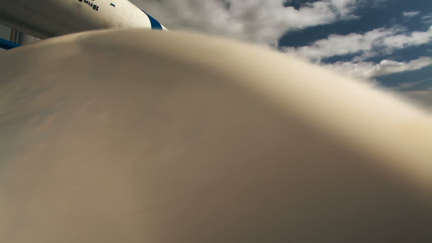 Wide dolly reveal of the lengthy white pipes running along the roof of a building at the IDE Ashkelon desalination plant in Israel, with billowing clouds and blue sky.