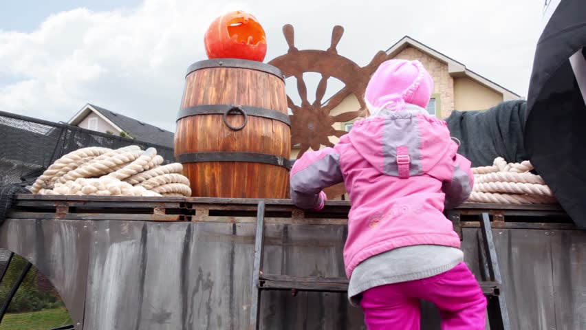 Little girl climbes by stairs on stage where is pumpkin of Halloween against ship scenery 