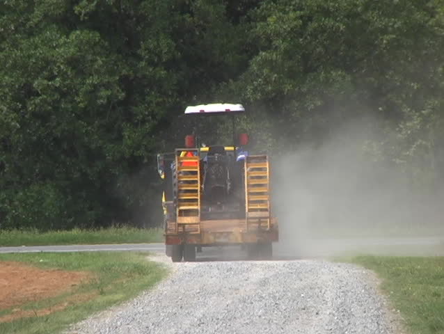 A heavy truck with trailer pulling a tractor pulls on to the highway and drives off.