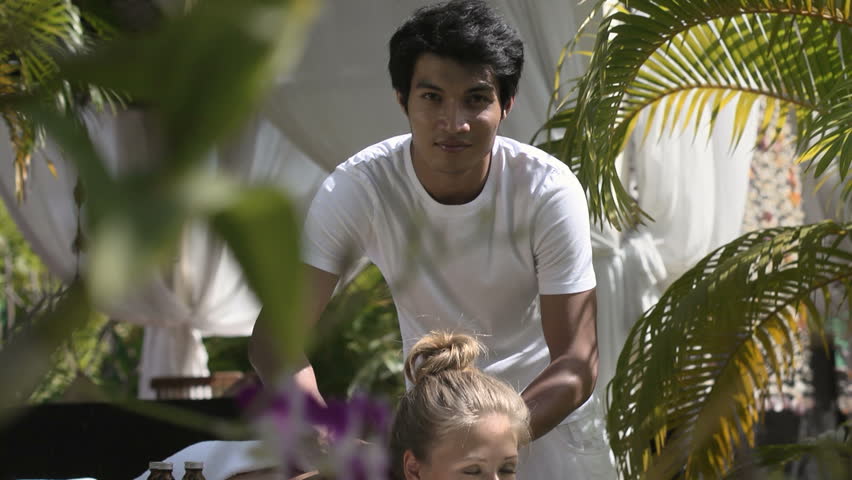Portrait of asian masseur giving massage to young beautiful blonde caucasian woman during beauty treatment in luxury spa