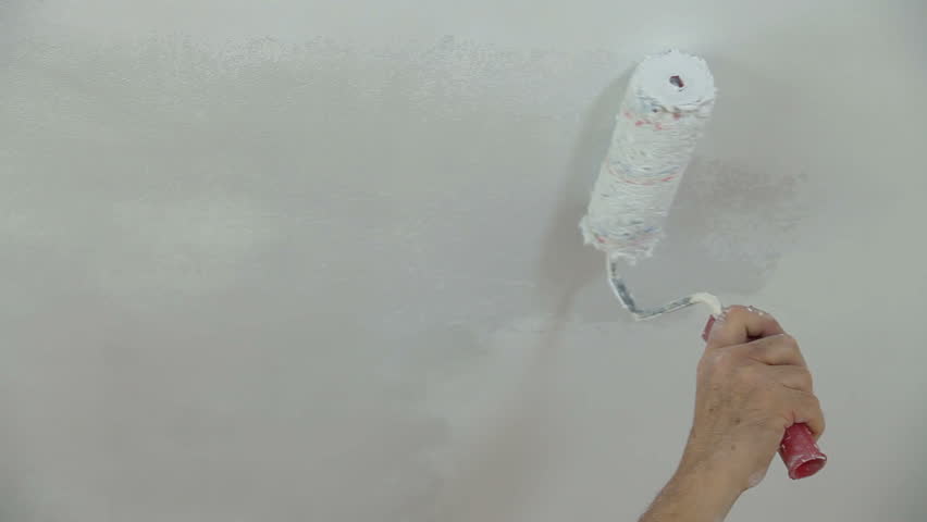 Hand holding a paint roller and painting ceiling Close-up