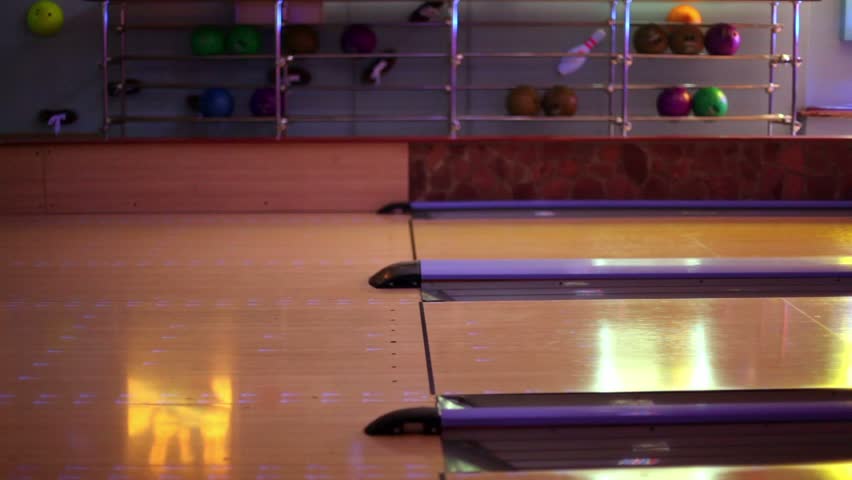 Two men throw bowling ball on parallel lanes in dark club, only legs are visible