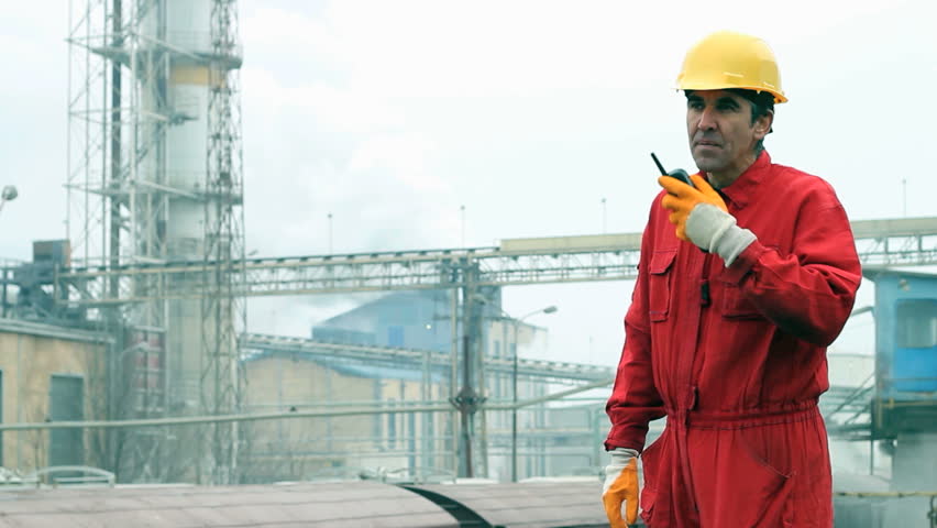 Factory worker in red overalls wearing hardhat and communicating over walkie-talkie. HD 1080i.