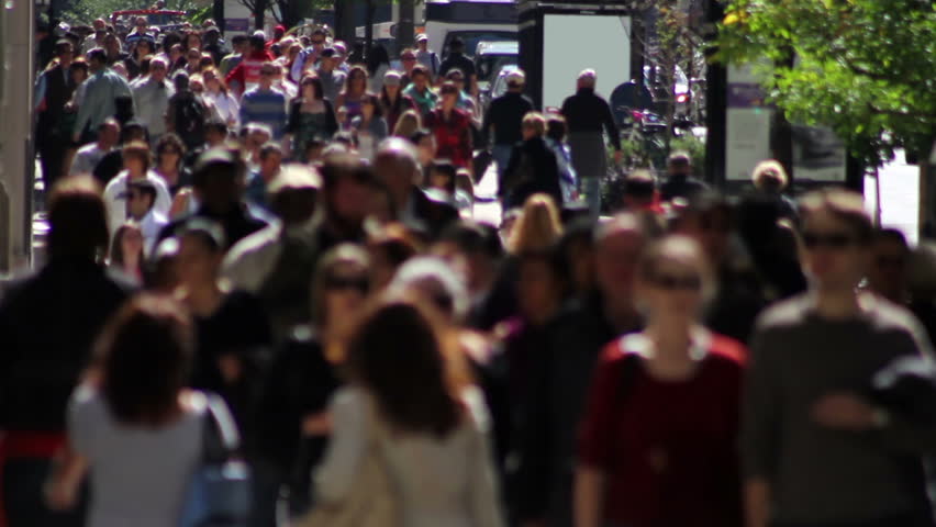 Telephoto shot with a backlit crowd of people on a wide sidewalk, walking in slow motion