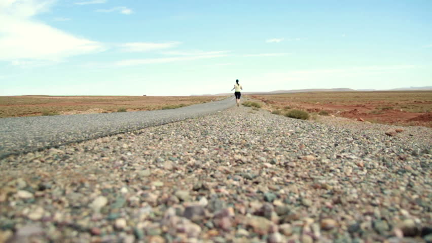 Young woman jogging on desert road, dolly shot, slow motion 