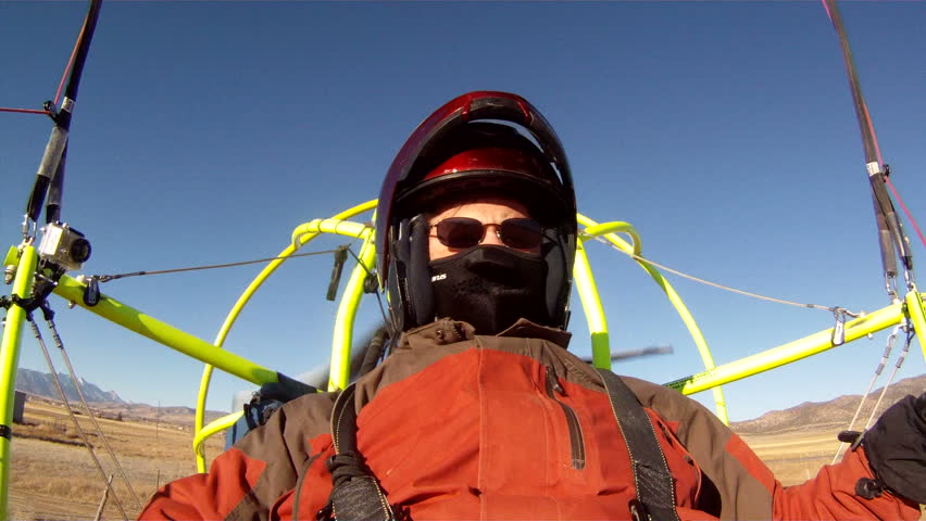 Pilot in an ultralight powered parachute aircraft flying landing in rough farm field farm land. Winter cold temperature wearing helmet and coat and gloves. Recreation and exciting way to travel.