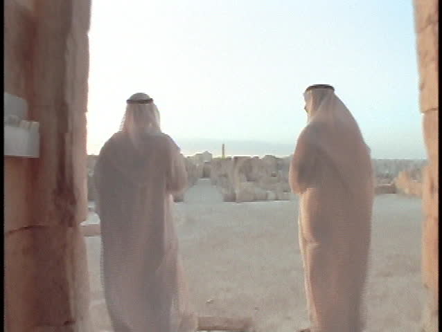 Saudi Arabian businessmen stand in front of an ancient ruin.