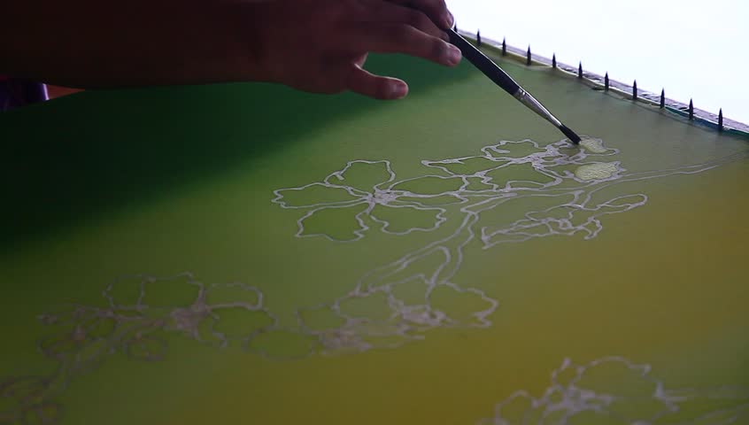 An artist carefully paint the floral/flower motif on a yellow traditional batik fabric