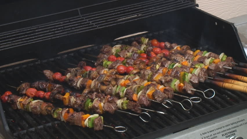 Colorful shish kebabs loaded onto white platter from backyard barbecue grill