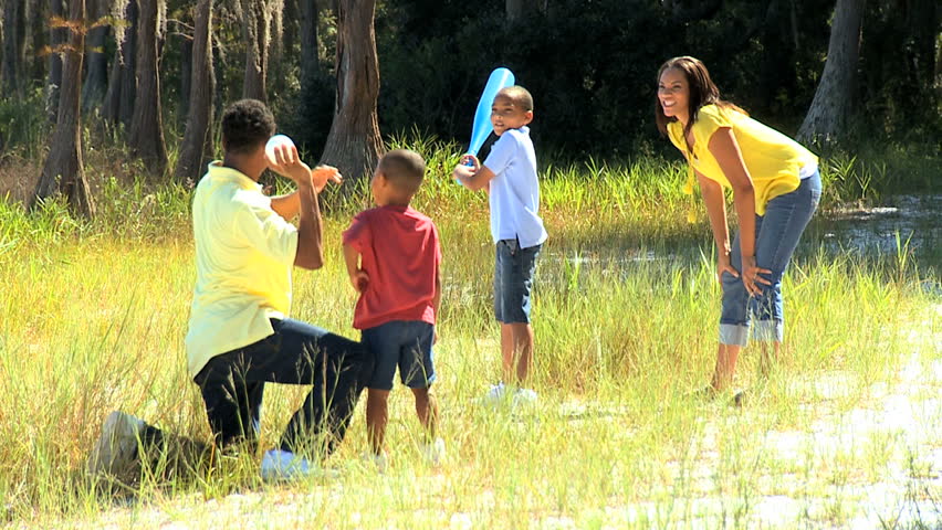 Healthy young ethnic family having fun playing baseball together in the park