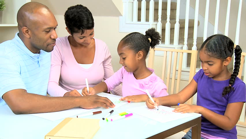 Young ethnic parents watching their young daughters using coloring crayons