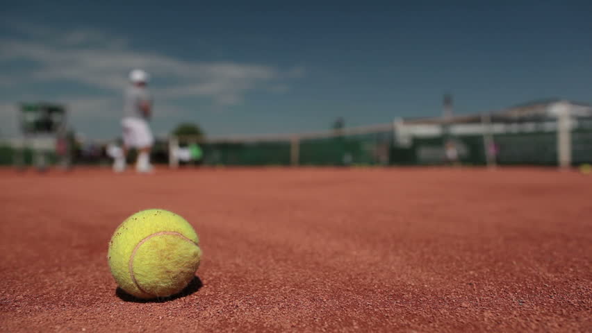 Tennis player (trainer) in action on tennis court (selective focus, focus on ball in the foreground) 