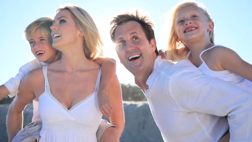 Attractive caucasian parents giving their children a piggyback on the beach