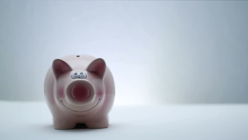 Hand is inserting a coin into pink piggy bank