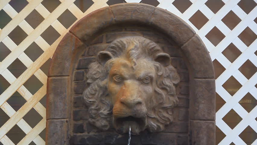 Lion head with water coming out of mouth in front of white lattice fence