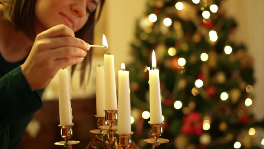 Young woman lighting a candle, christmas tree in background