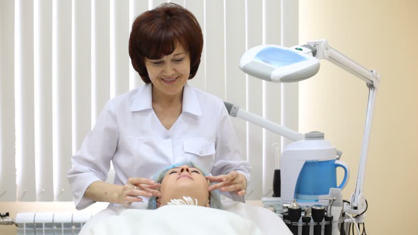 Woman receives facial massage in beauty shop from beautician