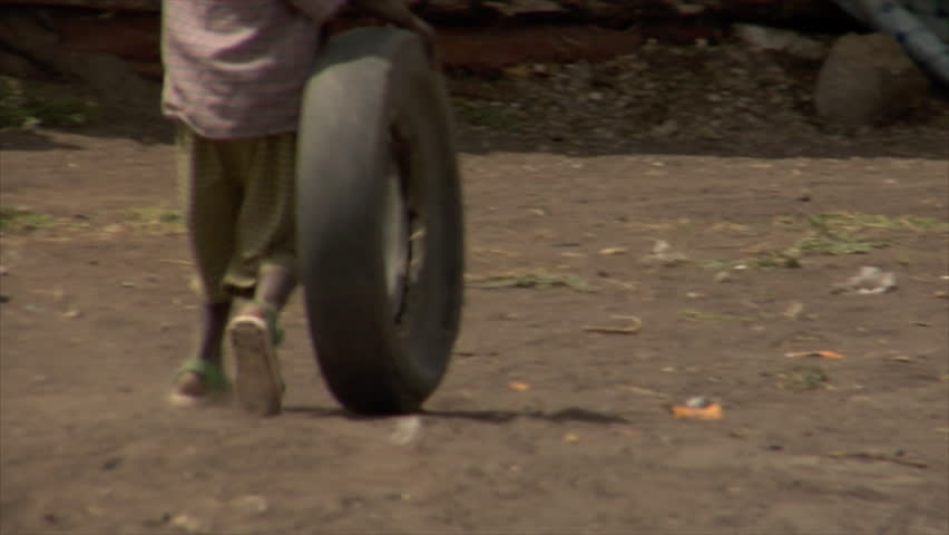 KENYA - CIRCA 2006: Unidentified African boy rolls a tire down a dirt road circa 2006 in Kenya.