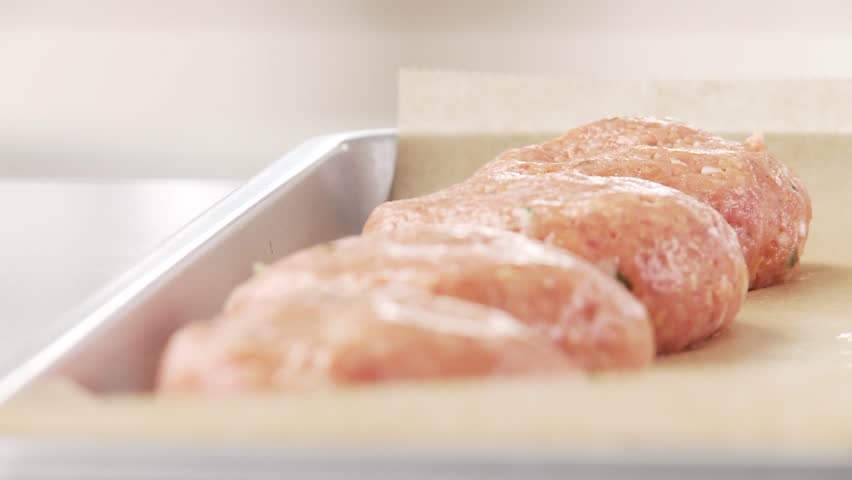 Raw burgers being placed on a baking tray laid with grease-proof paper