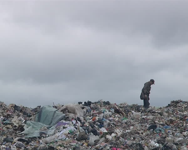 homeless man walking along the garbage heap in dump. poverty. environmental pollution.
