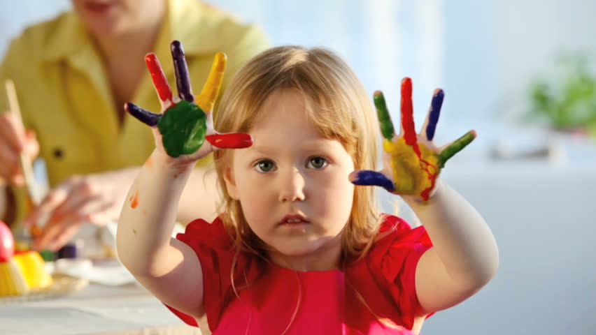 Little girl with fingers and palms painted in multicolors looking cheerfully at camera and dancing