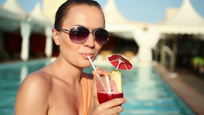 Happy woman drinking exotic cocktail by swimming pool
