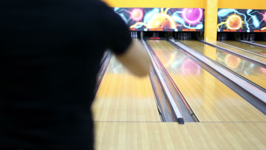 Young guy throws bowling ball and beats all skittles, view from behind