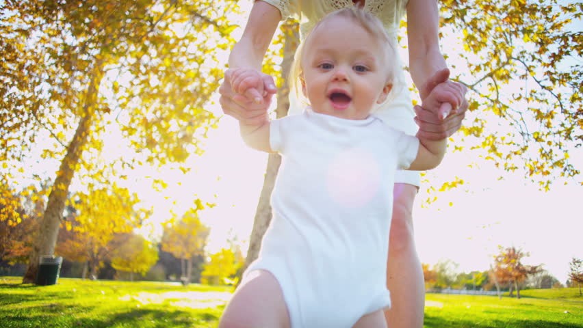 Caucasian mother supporting her little baby as she practices her first steps