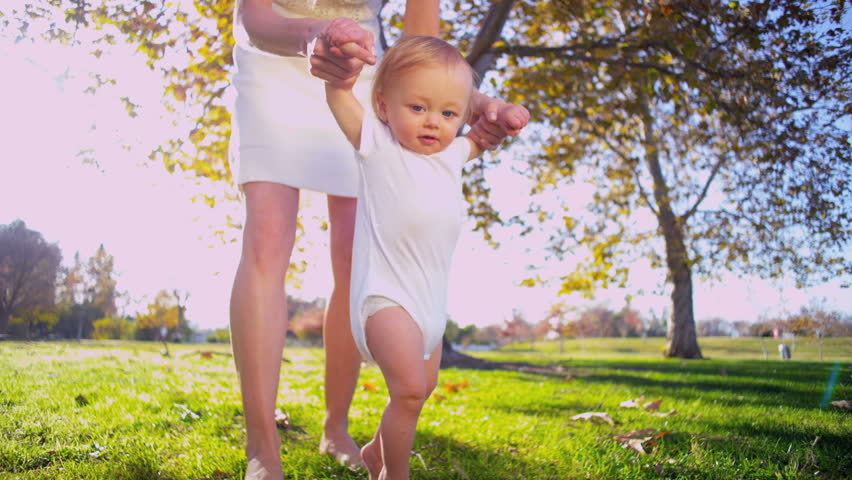 Caucasian mother supporting her little baby as he practices his first steps