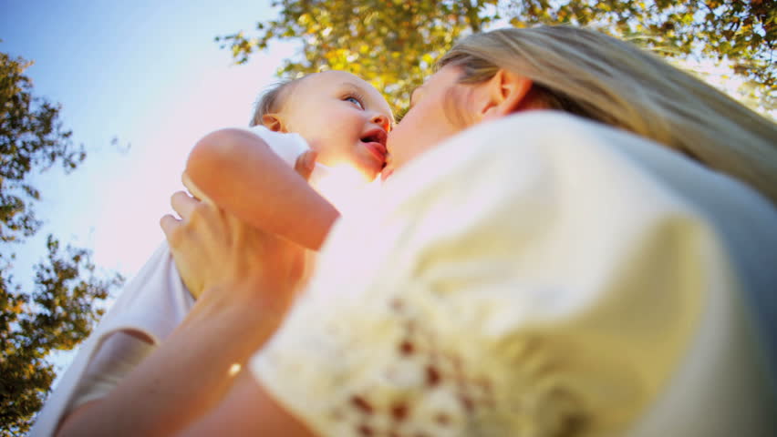 Blonde young mother and baby exchange a tender kiss as they play together outdoors