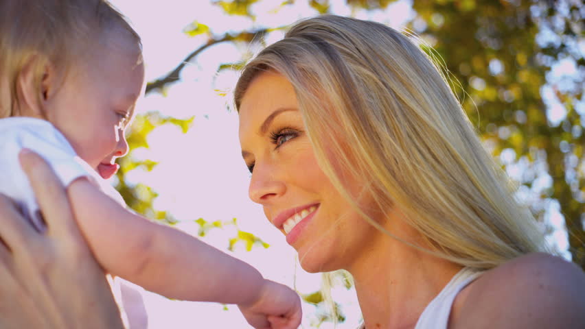 Young Caucasian mother holding her baby in the sunshine outdoors