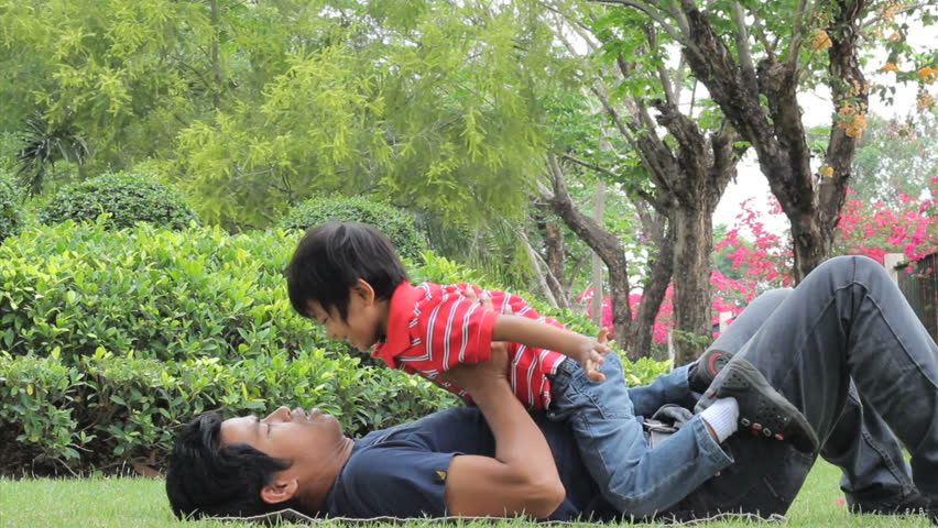 A loving father gives his cute Asian son an airplane ride as they spend time together at the park.