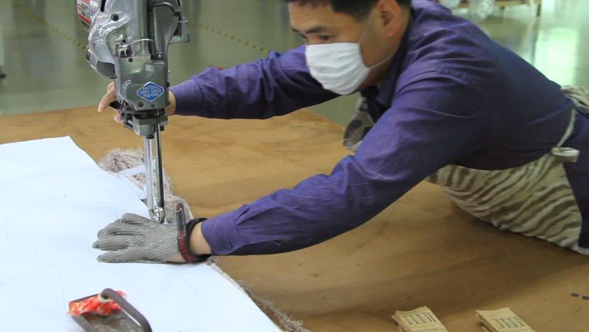 SHENZHEN, CHINA -  JUNE 5: male chinese textile factory worker cutting large pile of fabric. June 5, 2011 in Shenzhen, China