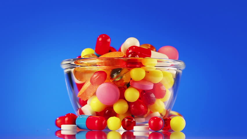 Pills, tablets and drugs in glass bowl rotating on blue background with copyspace - 2 views, loop ready