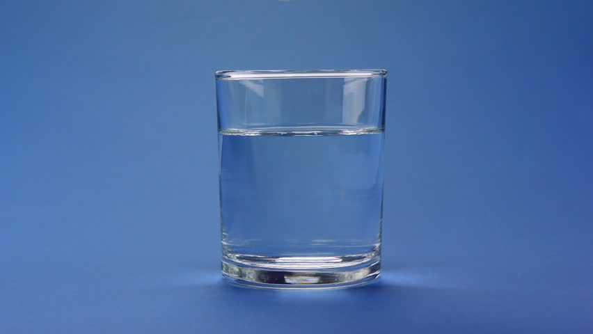 Aspirin or effervescent pill dropping into a glass of water on blue background.