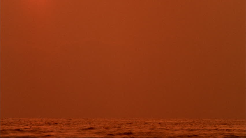 Sunset over Black Ocean Time-lapse - The sun slowly sets over the water as it pierces through smog and black sky.