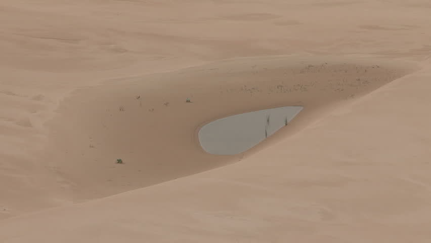 Wide and close up of desert dunes with small pool of water in the middle