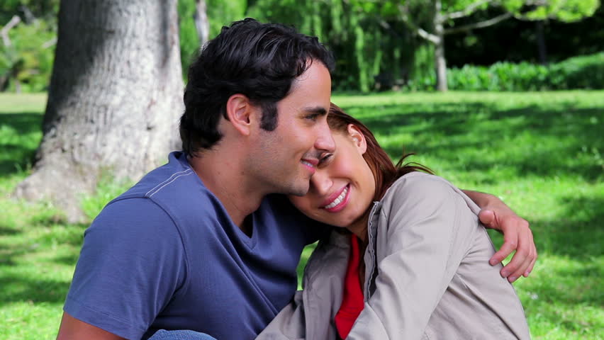 Smiling couple hugging each other while sitting on the grass in a parkland