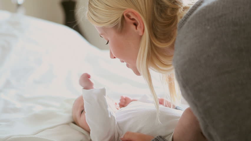 Woman holding and rubbing an energetic baby who is moving his arms and legs as he lies on a white bed