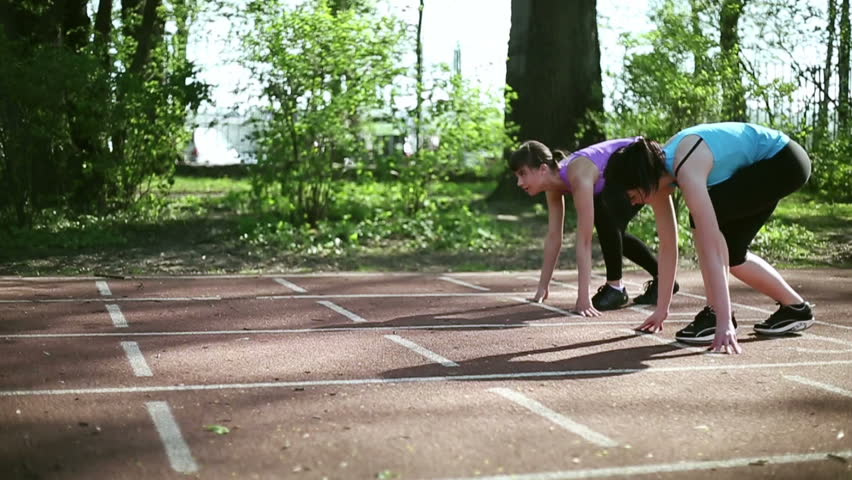 Two young women running on track lane, slow motion, dolly shot
