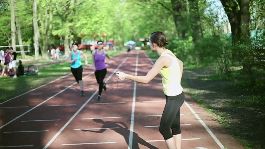 Women running on the track, trainer checking their time, slow motion
