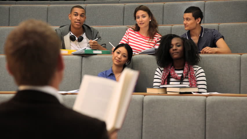 Teacher in front of students in lecture theatre reading literature