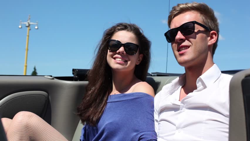 Young couple in sunglasses sit and talk in cabriolet at sunny summer day