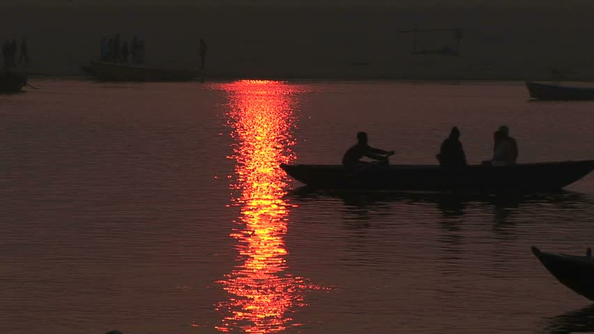 sun reflection on water as pilgrim boats row through and others are on far shore as boats pass, Veranasi, India